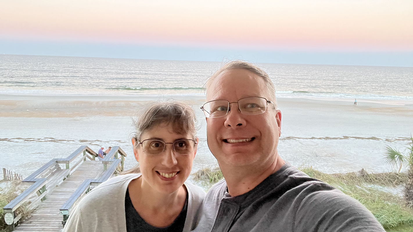 James and Julie with the color of a sunset over the water behind
