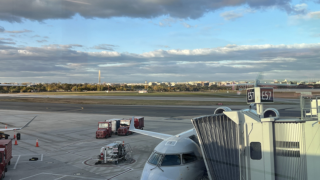 The Washington Monument rises above buildings beyond the taxiways of an airport