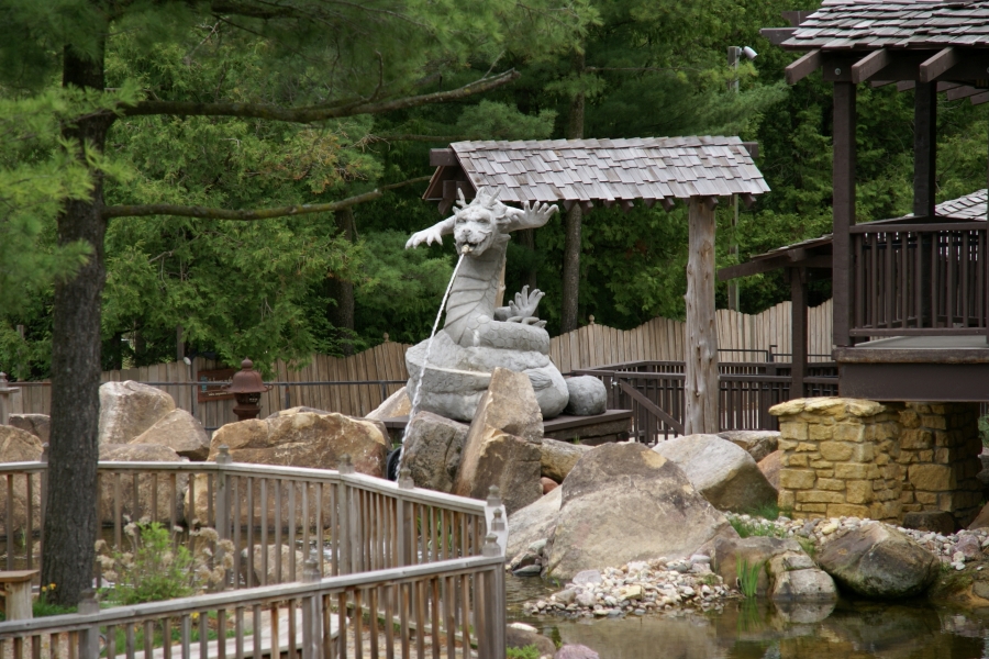 A concrete fountain shaped like a dragon sits on rocks and spits water into a pond