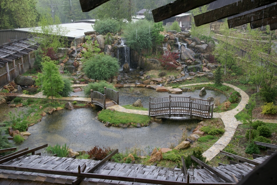 Rain falls into a different courtyard with two arched wooden bridges to a small island with a built up rock pile used to create cascading waterfalls